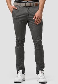Pantalones gris ajustados de algodón, con una cinturilla texturizada y un cinturón con patrón, combinados con zapatillas blancas.