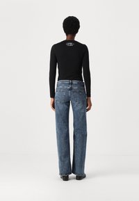 Svart langermet topp og lyseblå, høy midje, vide bukser med en falmet denimtekstur og baklommer, satt mot en ensfarget bakgrunn.