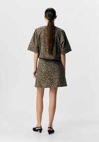 Leopardmönstrad kort klänning med vida ärmar och en figursydd midja, tillverkad av textil med struktur. Har längd ovanför knäna och svarta skor.