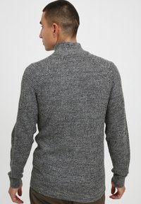 Grå strikket sweater med høj krave, ribbede manchetter og tekstureret overflade, set fra ryggen, der viser det generelle tætsiddende design.