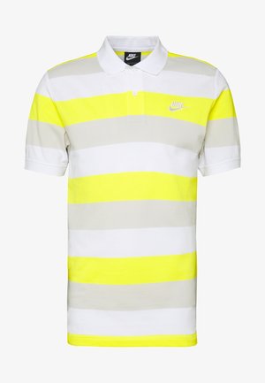 Polo en tissu texturé avec un col, affichant des rayures horizontales en jaune vif, gris et blanc. Logo Nike sur la poitrine.