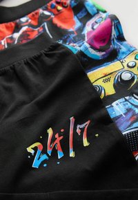 Schwarze Shorts mit buntem Grafikdesign und lebhaften Mustern. "24/7" in mehrfarbiger Schrift auf der Vorderseite gedruckt.