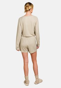 Beige Schlafanzugset mit langärmligem Oberteil und Shorts, ausgestattet mit einem strukturierten Diamantmuster. Kombiniert mit knielangen, gestrickten, cremefarbenen Socken.