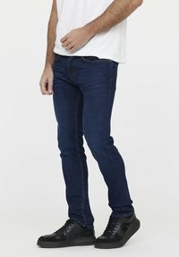 Jean slim bleu foncé en denim, avec un design classique à cinq poches, des détails de couture subtils et une taille mi-haute.