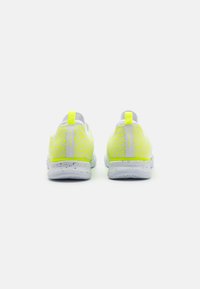 Vista posteriore di scarpe sportive con una tomaia in rete bianca decorata da un motivo giallo neon, linguetta di adozione e suola bianca maculata per una migliore aderenza.