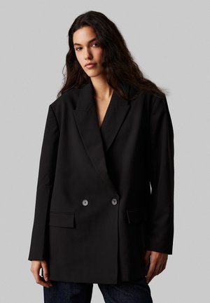 Blazer nero doppiopetto realizzato in un tessuto liscio, con rever a doppio spacco, due tasche frontali e dettagli con bottoni.