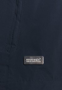 Tissu bleu marine foncé avec une couture verticale et un petit badge métallique rectangulaire argenté portant l'inscription "Regatta Great Outdoors".