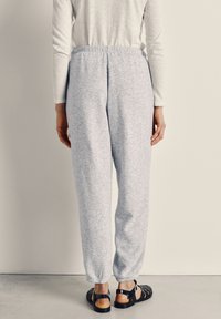 Light gray, textured sweatpants with an elastic waistband and cuffs. Worn with black sandals, viewed from the back.