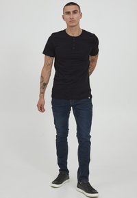 Black short-sleeve henley t-shirt with three buttons, paired with dark denim jeans and black sneakers, set against a neutral background.