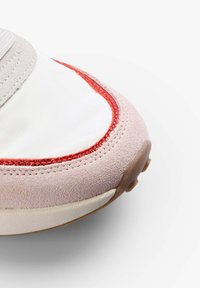 Tenisky s texturovaným, světle růžovým semišovým svrškem, bílou textilní vložkou a kontrastním červeným prošíváním podél okraje špičky.