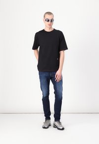 Czarny t-shirt z krótkim rękawem z kontrastowymi czerwonymi przeszyciami, zestawiony z niebieskimi dżinsami i szarymi butami sportowymi. Dodatki to refleksyjne okulary przeciwsłoneczne.