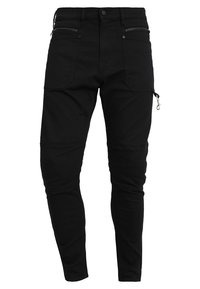 Pantalones cargo negros hechos de una mezcla de materiales de algodón, que cuentan con múltiples bolsillos, detalles con cremalleras, corte tapered y costuras visibles.