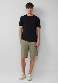 Zwarte t-shirt met korte mouwen en een borstzak, gecombineerd met licht olijfgroene knielange shorts en beige sneakers. Eenvoudig ontwerp, casual pasvorm.