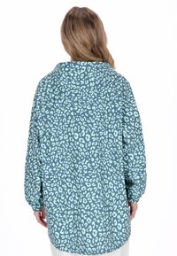 Una chaqueta con capucha de estampado de leopardo en color verde azulado, con un ajuste holgado y mangas largas, que presenta un patrón texturizado con manchas en menta contrastantes.