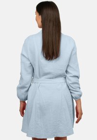 Abito avvolgente azzurro chiaro in tessuto testurizzato. Caratterizzato da maniche lunghe, vita con cintura e gonna a campana. Design semplice ed elegante.