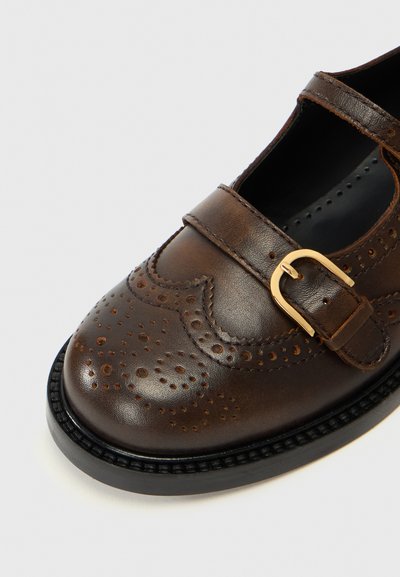Bruine leren schoen met geperforeerde details en een gouden gesp. Heeft een ronde neus en een gestructureerde zwarte zool.