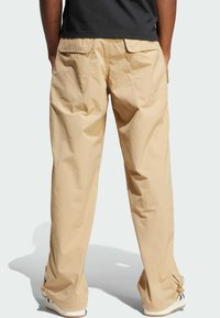 Pantalons cargo beiges avec une coupe décontractée, deux poches arrière et des ourlets ajustables, fabriqués à partir d'un matériau léger.