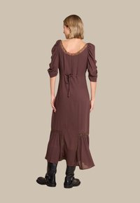 Brun maxi kjole med pufferm, en blondebesatt halslinje og knytning bak, med lagdelte skjørt detaljer og parret med svarte ankelstøvler.