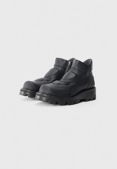 Botas de cuero negro hasta el tobillo con un acabado texturizado, cremallera lateral y suela de goma gruesa con tacos profundos para mayor agarre.
