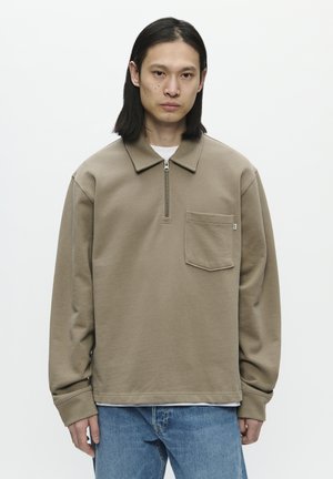 Brown zip-up sweatshirt with a collar, front pocket, and long sleeves. Distressed blue jeans complete the outfit.