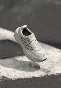 Baskets de sport beige clair avec une tige en mesh, un design courbé et des accents bleus contrastants. Présente un logo "Fresh Foam" bien visible sur la semelle.