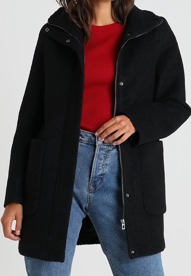 Svart ullblandad kappa med dragkedja fram, stora fickor och huva. Bärs över en röd ribbad topp och ljusblå denimjeans.