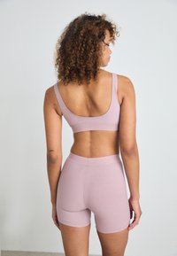 Set di abbigliamento sportivo rosa chiaro composto da un reggiseno a coste e pantaloni corti abbinati. Tessuto liscio e elasticizzato con cuciture minime e vestibilità aderente.