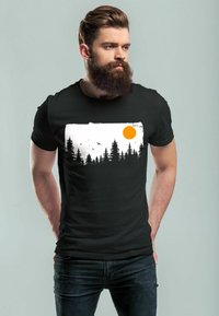 Schwarzes T-Shirt mit einem weißen Grafikdesign von Bäumen, einer Sonne und Vögeln, das ein mutiges Design mit matter Textur zeigt.