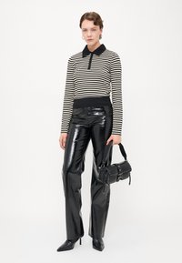 Czarna i biała w paski long-sleeve polo, spódnie typu high-waisted z błyszczącego czarnego materiału oraz mała czarna torebka z detalami w postaci ćwieków.