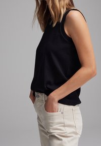 Black sleeveless top with a smooth texture, round neckline, and relaxed fit, paired with light beige trousers with side pockets.