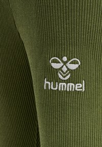 Olivgrön ribbad tyg med en broderad vit logotyp som föreställer ett stiliserat insekt och varumärkesnamnet "hummel" på vänster sida.