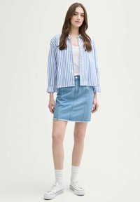 Gestreepte blauw-witte button-up overhemd gecombineerd met een lichtblauwe spijkerrok met uitlopende zoom. Witte sneakers en sokken maken de look compleet.