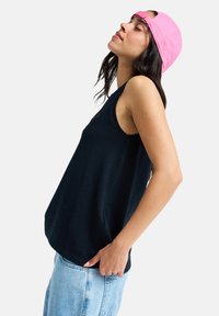 Μπλε ναυτικό αμάνικο τοπ με άνετη εφαρμογή, σε συνδυασμό με ανοιχτόχρωμο μπλε τζιν. Ένα ροζ καπέλο μπέιζμπολ ολοκληρώνει το casual look.