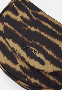 Levi's pussukka, jossa on ruskea ja musta tiikerinraidallinen kuvio, kangasmateriaali ja kohokuvioitu logo sileällä pinnalla.