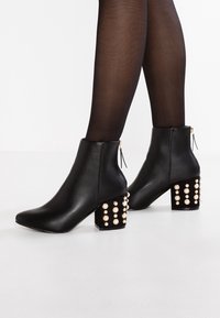 Schwarze Leder-Stiefeletten mit spitzem Zeh und dekorativen Perlenakzenten auf einem klobigen Absatz. Verfügt über einen seitlichen Reißverschluss zum Schließen.
