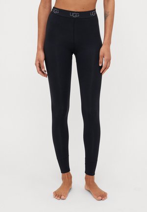 Leggings noirs en matériau lisse et extensible, avec une taille haute arborant le logo "UGG" dans une couleur contrastante.