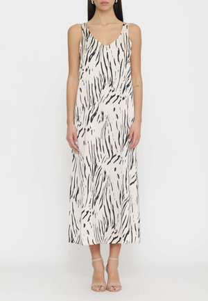 Donna che indossa un abito midi senza maniche con stampa zebra bianco e nero, scollo a V e décolleté beige con cinturino alla caviglia, in piedi contro uno sfondo neutro.