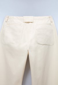 Light beige pants with a smooth texture, featuring a waistband label, two back pockets, and a straight-leg design.