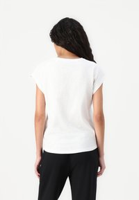White short-sleeve t-shirt with a soft texture, rounded neckline, and discreet side slits, paired with black trousers.