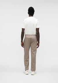  Ανοιχτό γκρι εφαρμοστό T-shirt και μπεζ φόρμα με ελαστική μέση, πλαϊνές τσέπες και μία πίσω τσέπη, σε συνδυασμό με λευκά αθλητικά παπούτσια.