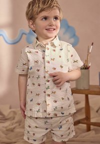 Set di camicia a maniche corte e pantaloni corti realizzato in tessuto cremoso strutturato, con motivi colorati di cani e fiori su tutta la superficie.