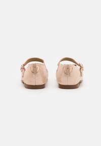 Scarpe flat rosa pallido con finitura testurizzata, dotate di una fascia con fibbia e un logo in rilievo a forma di cuore sul retro. Suola bassa marrone.