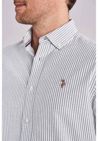 Koszula zapinana na guziki w szaro-białe paski, z małym haftowanym logo. Kołnierzyk z dwoma guzikami przy szyi. Materiał bawełniany.