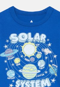 Mėlyna medvilninė marškinėliai su saulės sistemos grafika, vaizduojančia planetas, saulę ir žvaigždes pieštuko stiliumi. Apvalios iškirptės dizainas.