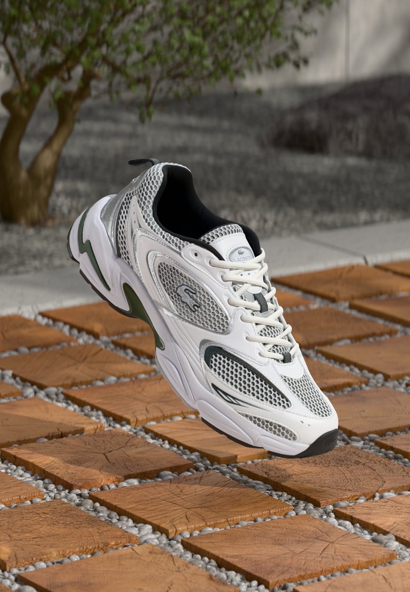 White athletic sneaker with mesh panels, black accents, and a thick sole. Features lacing system and logo on the tongue.