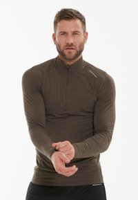 Bruine langemouwen sporttop met een ritskraag, aansluitend ontwerp en rekbare stof. Gedetailleerd met een logo op de schouder en ademende textuur.