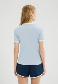Jasnoniebieska sportowa bluzka z krótkim rękawem i kremowymi detalami; dopasowany krój; miękka tkanina; w zestawie z ciemnoniebieskimi szortami z białymi akcentami.