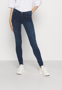 Jeans ajustados de color azul oscuro con detalles acanalados en las rodillas, confeccionados en denim, que cuentan con cinco bolsillos y un diseño entallado.