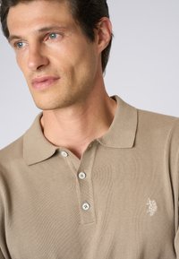 Polo shirt beige con un motivo a maglia testurizzata, colletto classico, tre bottoni e un piccolo logo ricamato sul lato sinistro del petto.