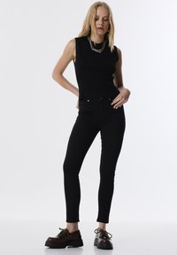 Zwart geribbeld mouwloos topje gecombineerd met aansluitende zwarte jeans en bruine veterschoenen met een dikke zool en een textuurafwerking.